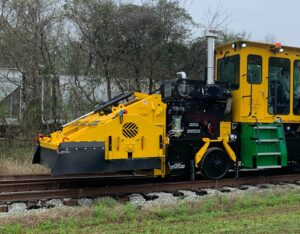 The KBR 925 Broom attachment with insulated broom box on railway tracks and rail cars behind.