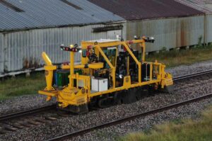 KKA 1050 on railway tracks with manufacturing plant in background.