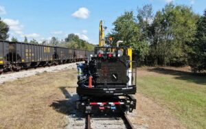 Back end view of KTC 1250 tie crane on railroad tracks with other railroad cars on the left.